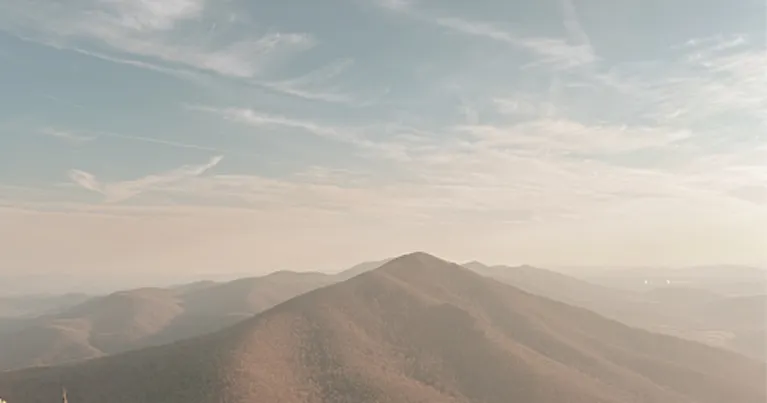Panoramic view of a mountain range under a lightly cloudy, pale blue sky.
