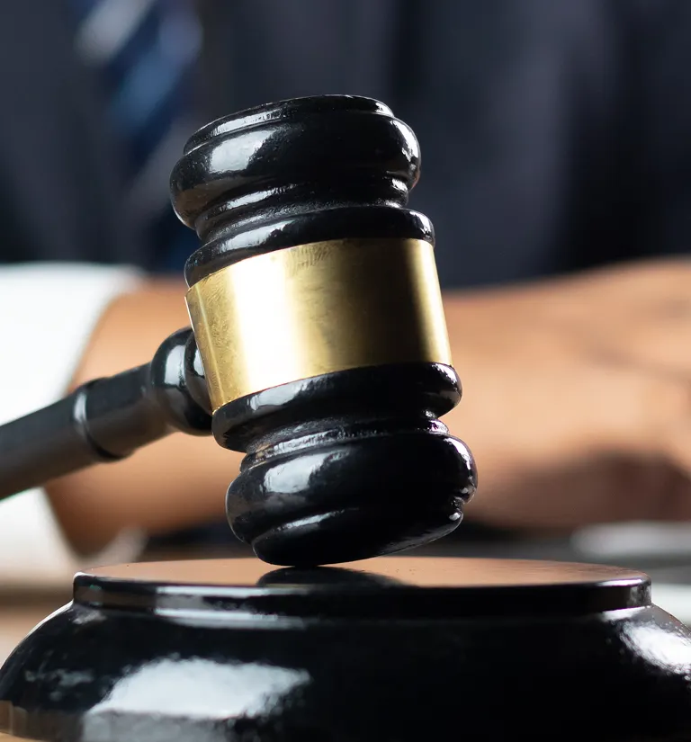 Close-up of a black wooden judge's gavel with a gold band, held above a sound block.
