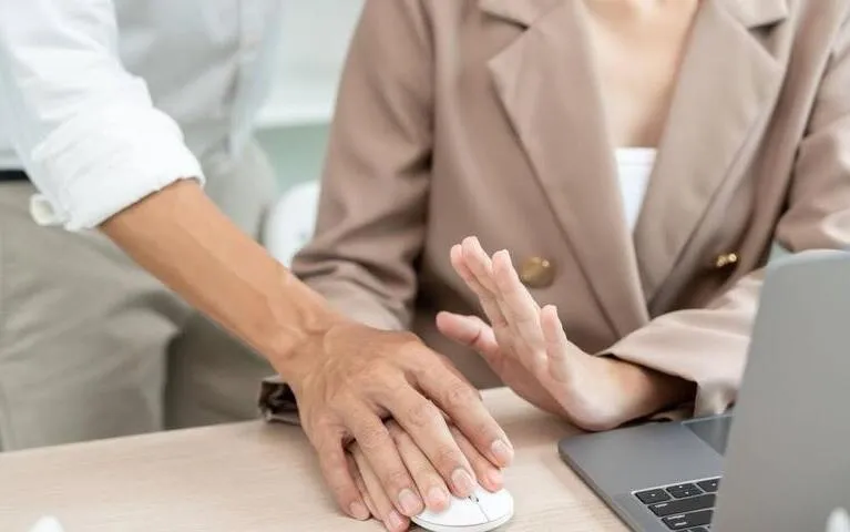 A person in a beige blazer raising their hand to stop another person's hand on a computer mouse.
