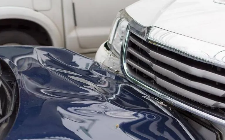 Close-up of a white car and a dark blue car involved in a front-end collision showing significant denting.