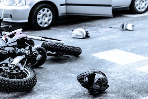 Motorcycle lying on its side with a black helmet and car in the background.