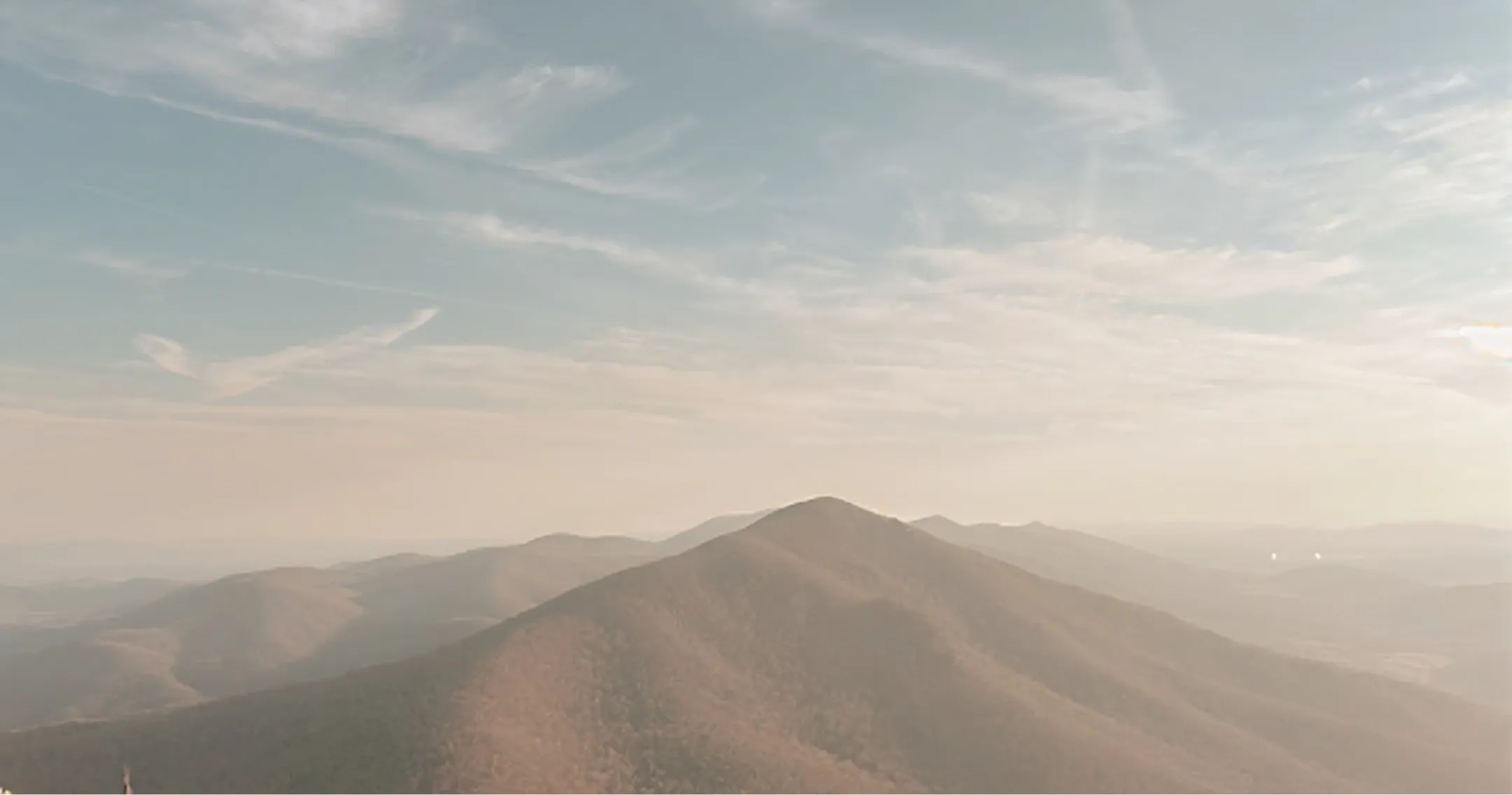 Mountain range under a partly cloudy blue sky with soft sunlight and distant peaks.