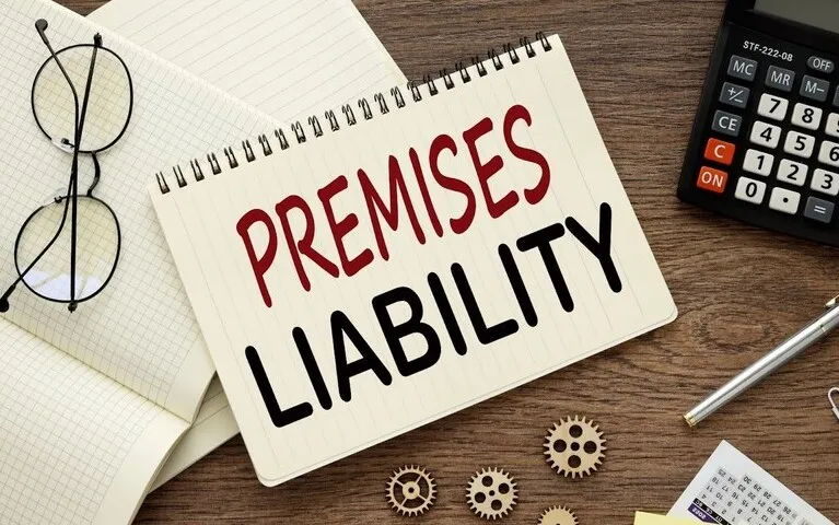 Spiral notebook with "Premises Liability" text, glasses, calculator, pen, and papers on wooden desk.