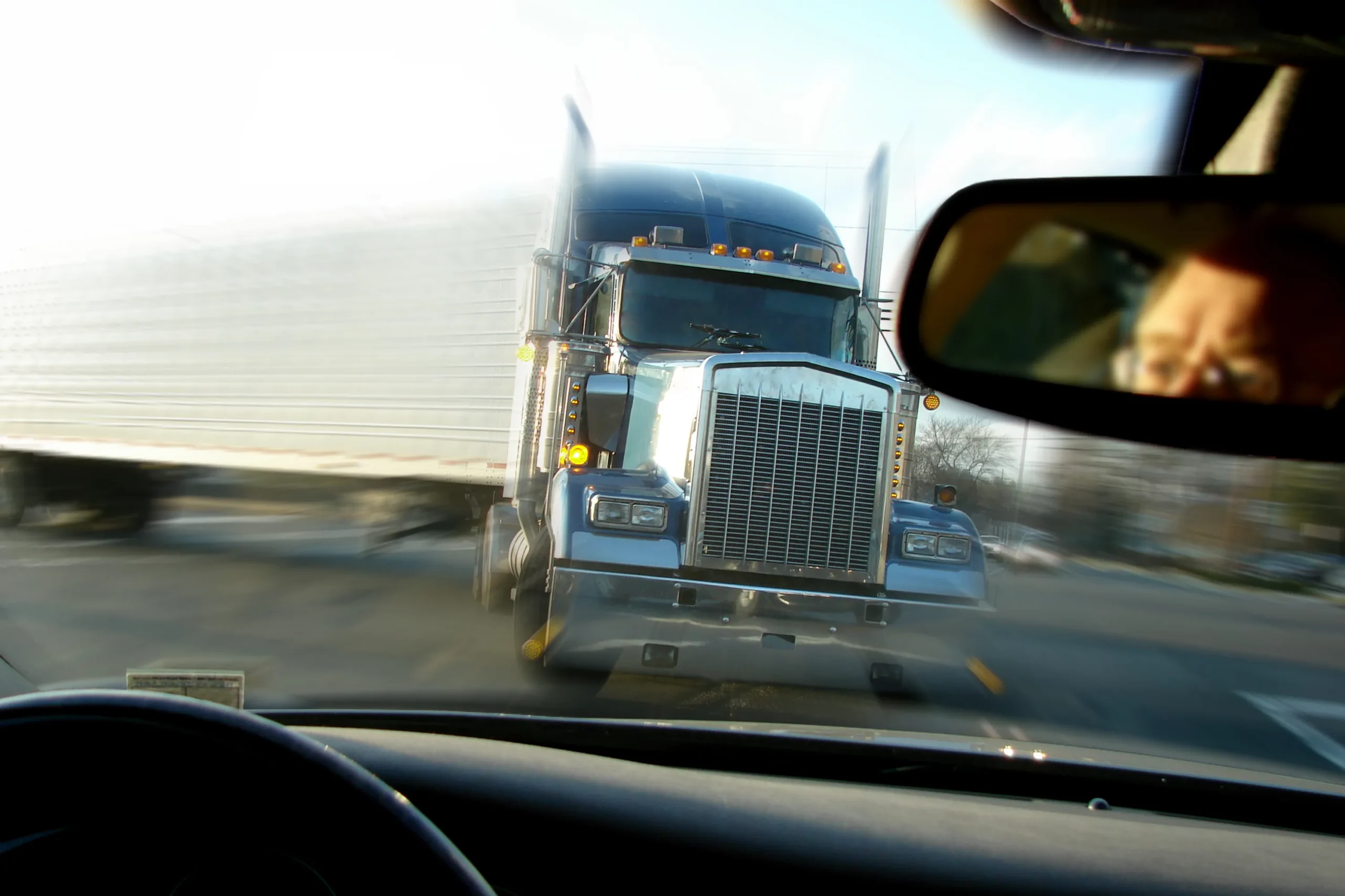 View from inside a car showing a large blue semi-truck approaching in the opposite lane.