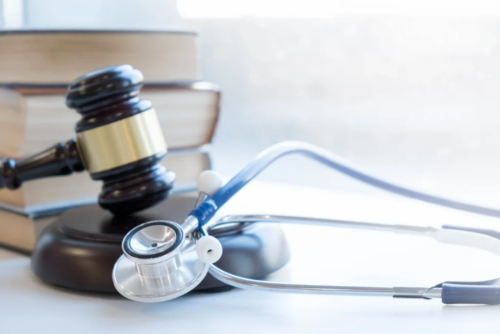 Wooden judge gavel, stethoscope, and stacked books on white surface background.