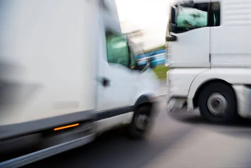 Blurred image of two white commercial trucks passing each other on a road.